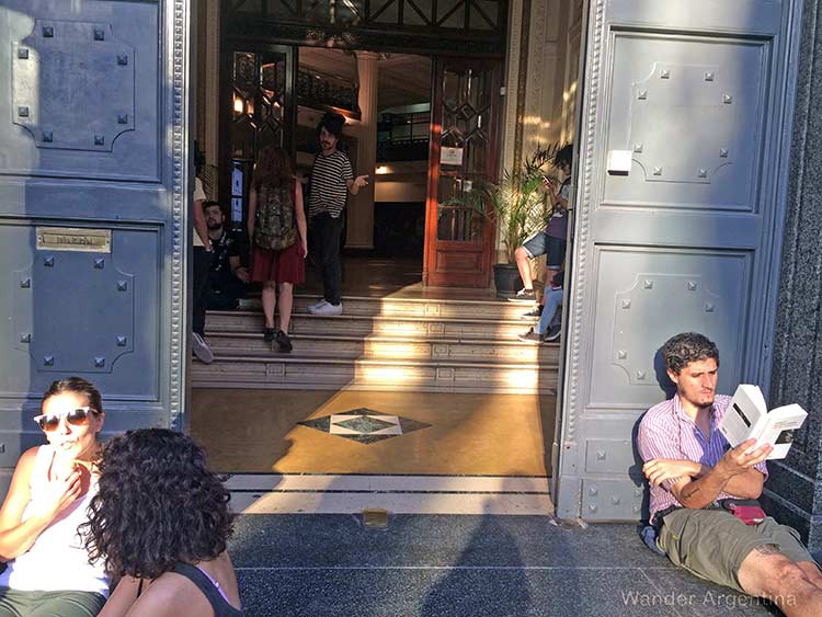 A group of students chat and one reads a book at the entrance to a university in Buenos Aires 